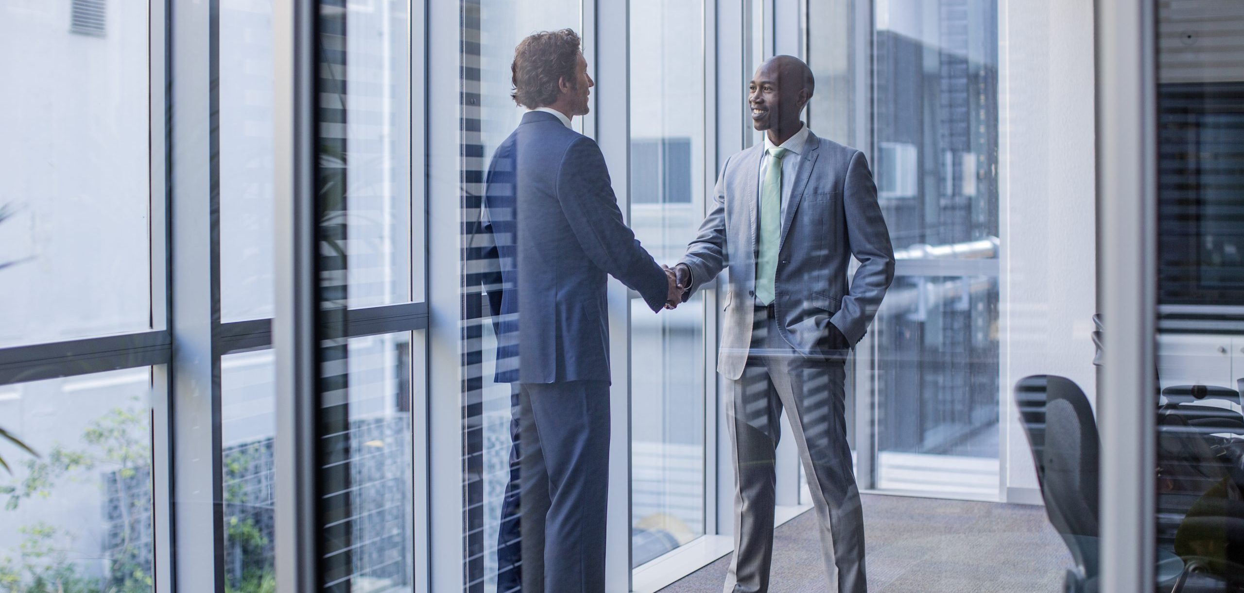 Full length of multi-ethnic businessmen shaking hands in office